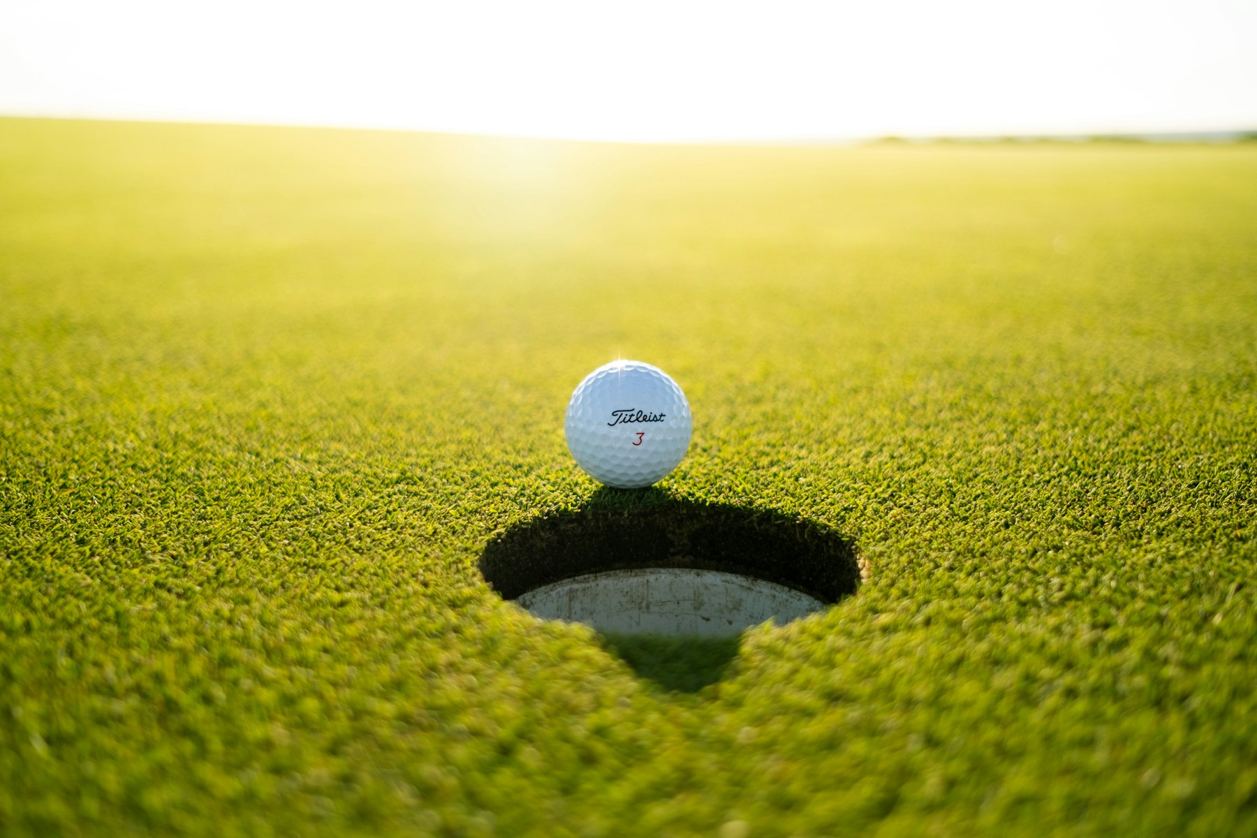 Golfball am Lochrand im warmen Abendlicht